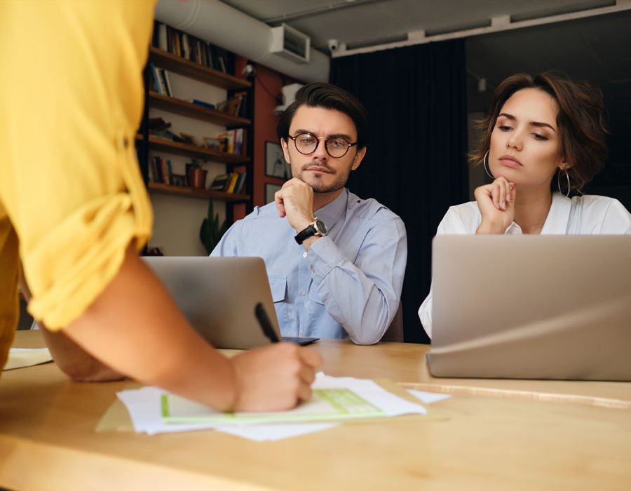 Group of business colleagues sitting at the desk with laptop thoughtfully working with papers in modern office